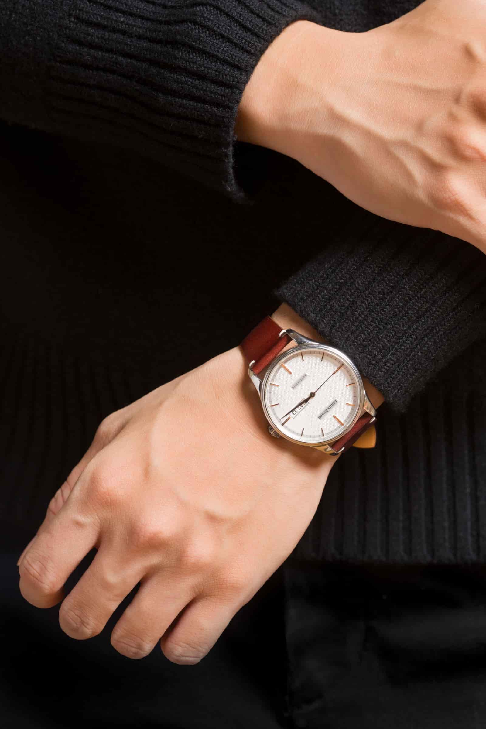 Oxblood calf leather watch strap worn on the wrist under a black knitted cuff, showing how the padded strap falls around the arm