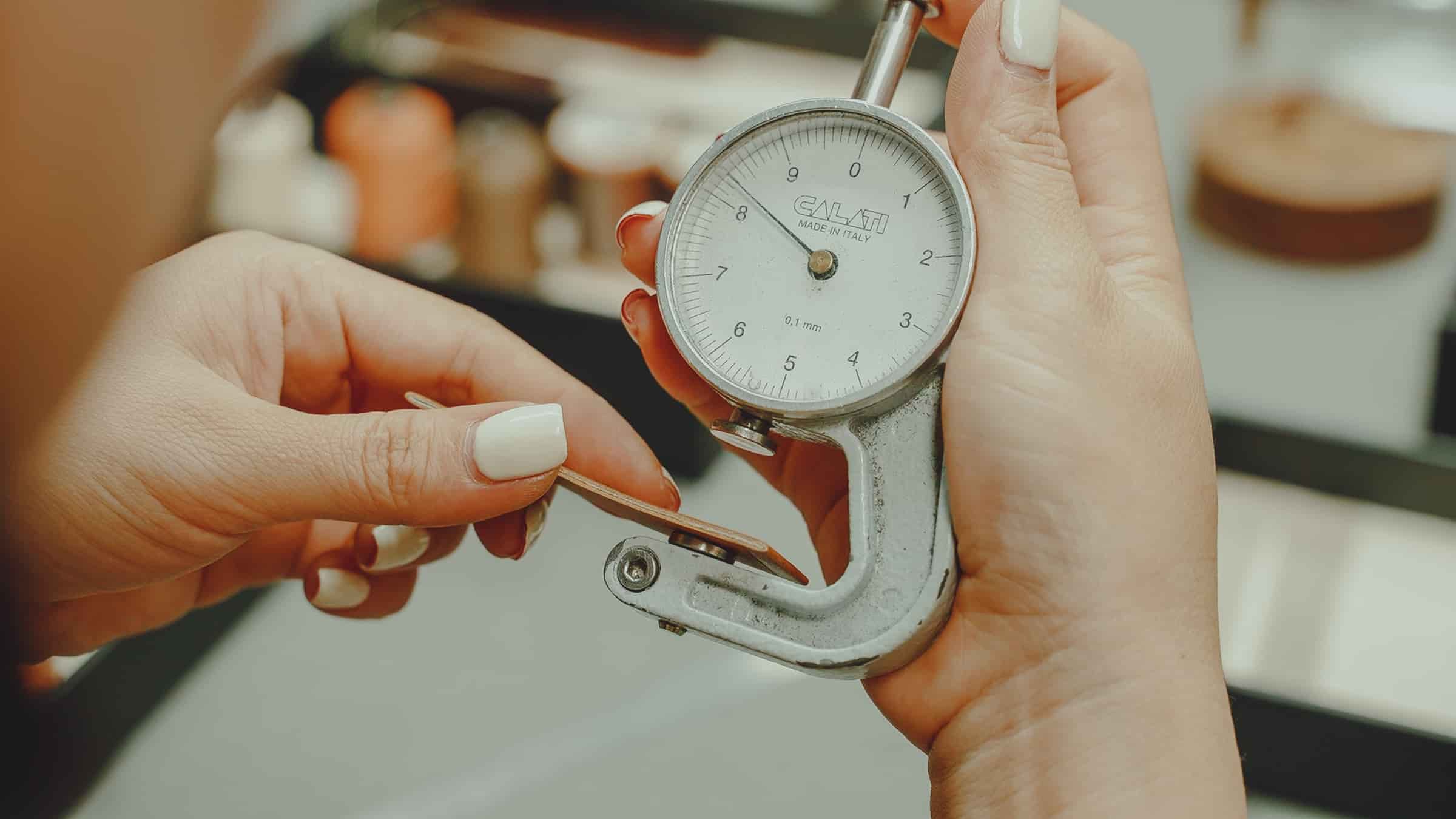 A dial thickness gauge being used to measure a finished leather watch strap during quality control at AKC
