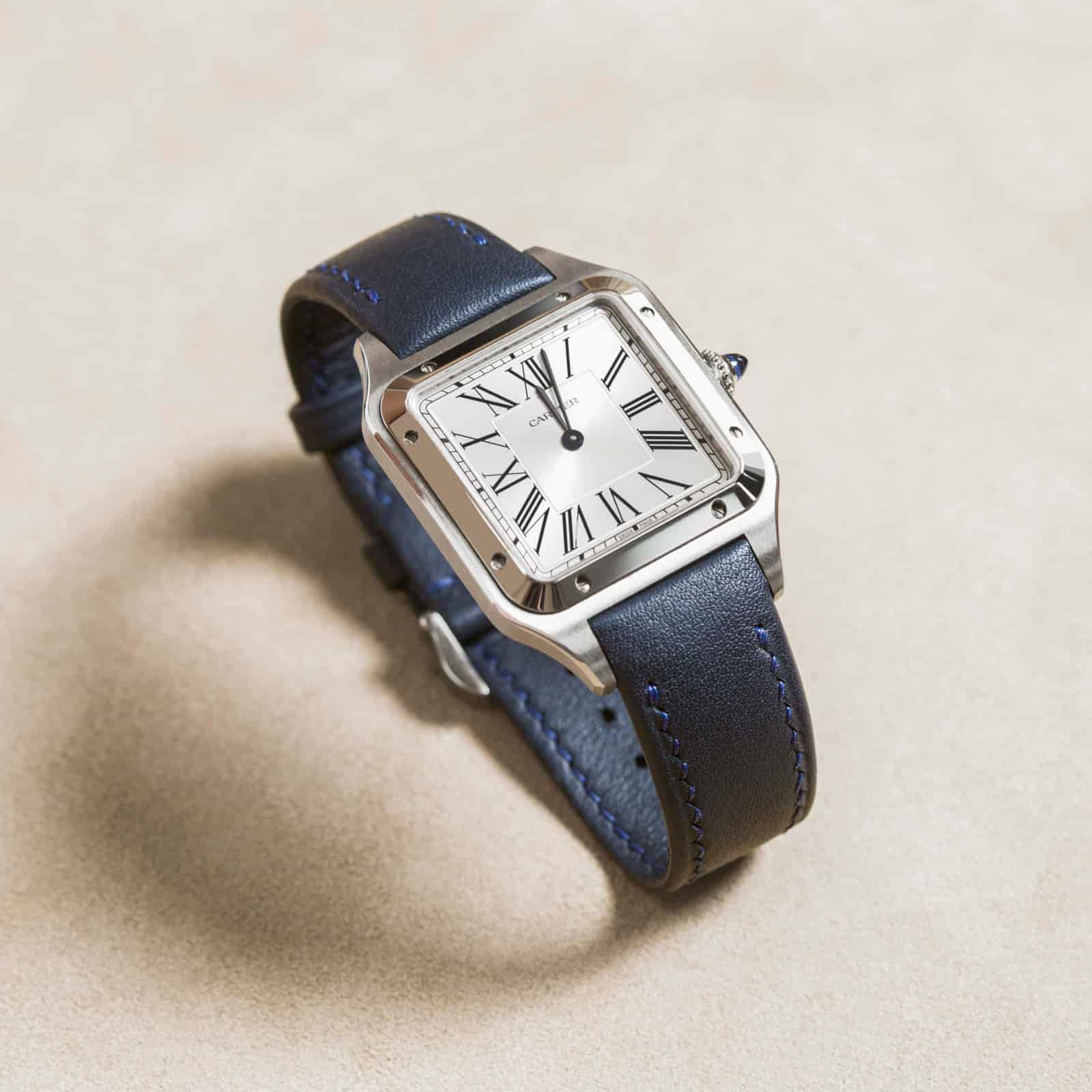 Navy calf leather watch strap on a square-cased dress watch, curled on bone-coloured suede so the integrated lug line reads end to end