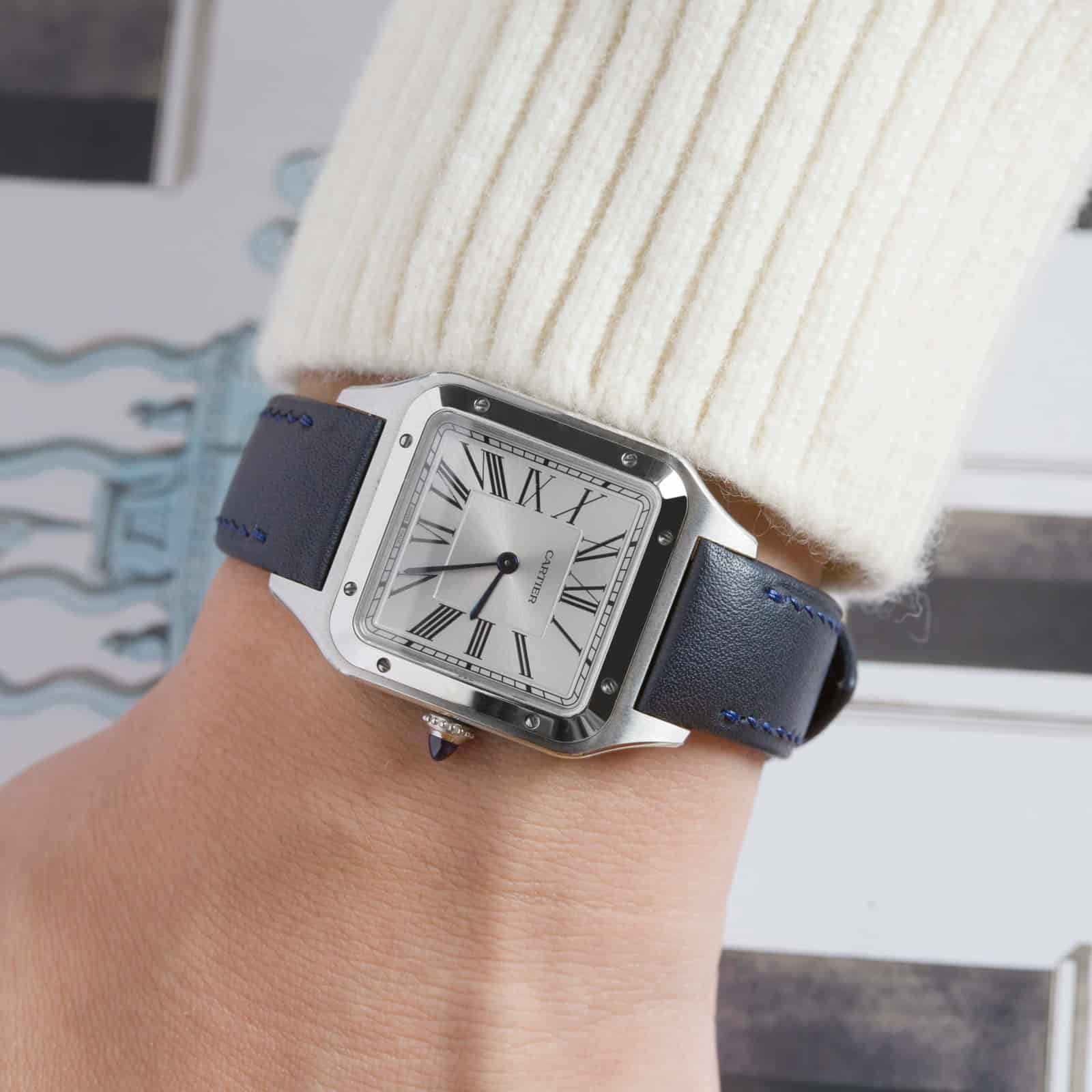 Navy leather strap on a square-cased watch worn on the wrist beneath a cream knitted sleeve