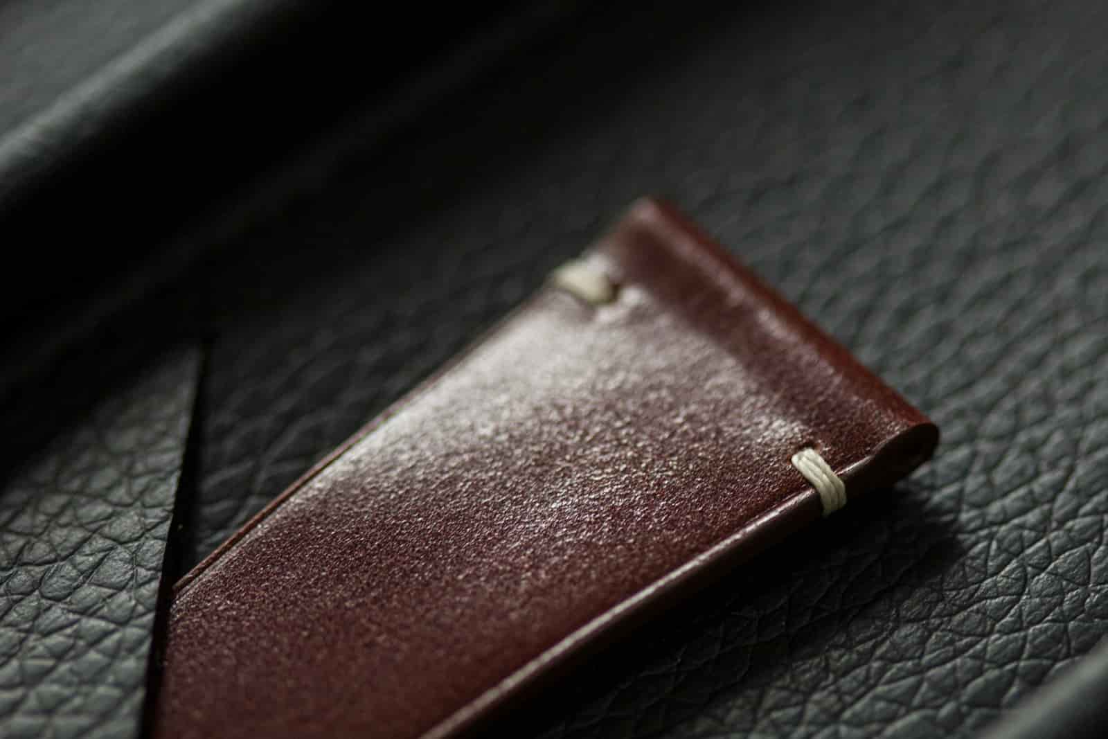 Oxblood shell cordovan watch strap tab photographed on black pebble-grain leather, showing two surfaces against each other, made by AKC