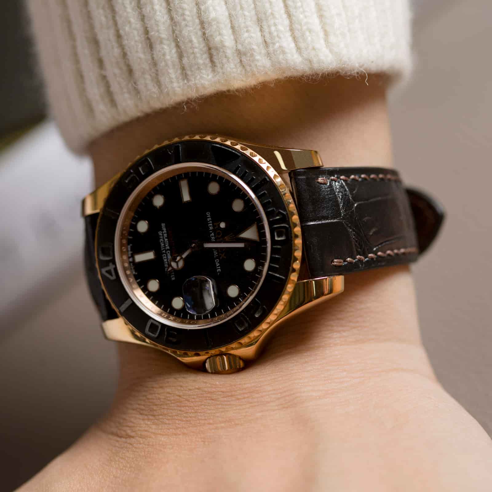 Black alligator leather watch strap on a gold-and-black dive watch worn on the wrist beneath a cream knitted sleeve