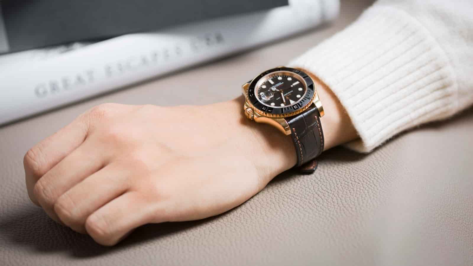 A hand at rest over an open book, wearing a dive watch on a dark leather strap, the strap falling naturally around the wrist